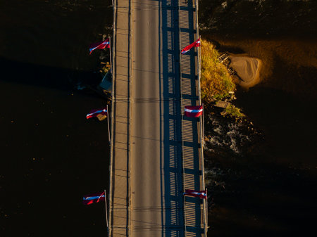 An aerial perspective captures a bridge with red, white, and blue flags over a dark river in...