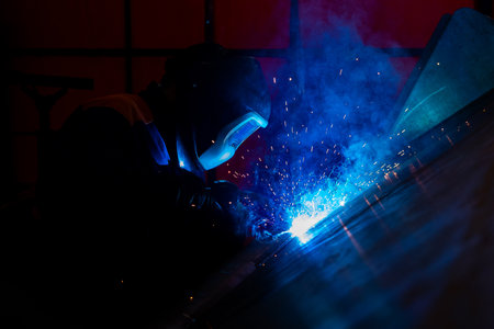 Skillful metal worker working with arc welding machine in factory while wearing safety equipment....