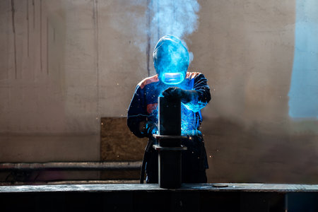 Skillful metal worker working with arc welding machine in factory while wearing safety equipment. Metalwork manufacturing and construction maintenance service by manual skill labor conceptの写真素材