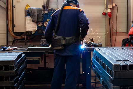 Welding work at a metalworking plant. A helmeted welder welds a metal part on a welding table