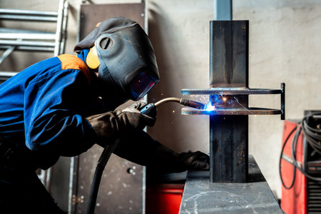 Welding work at a metalworking plant. A helmeted welder welds a metal part on a welding tableの写真素材