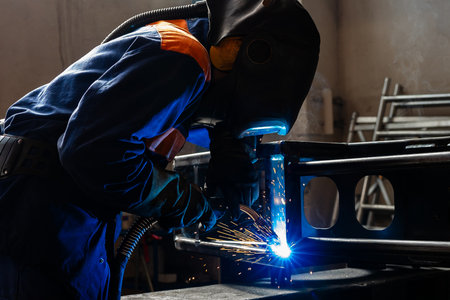 Welding work at a metalworking plant. A helmeted welder welds a metal part on a welding tableの写真素材