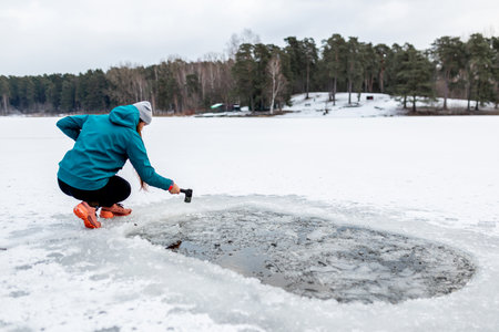 Winter swimming. A woman carving an ice hole entry in lake with axeの写真素材