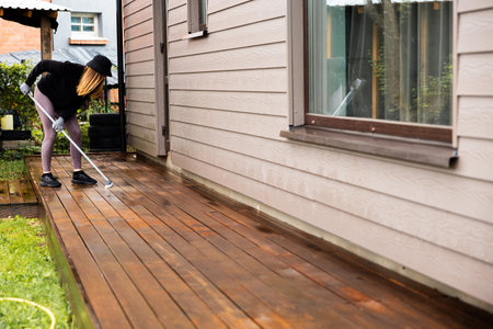 Woman washes a wooden terrace before painting it in her modern private houseの写真素材