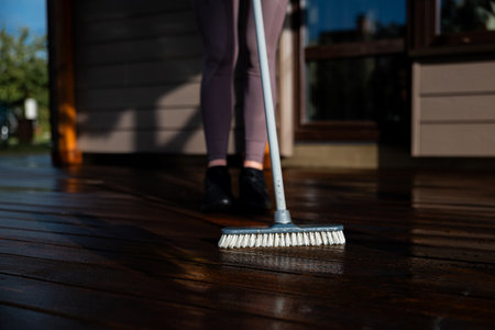Woman washes a wooden terrace before painting it in her modern private houseの写真素材
