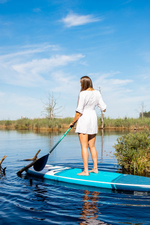 Beautiful young woman in white dress paddleboarding on the lakeの写真素材