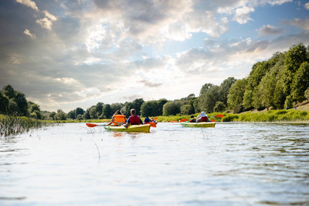 Group of friends kayaking enjoy trip down a scenic river with a dramatic cloudy sky aboveの写真素材