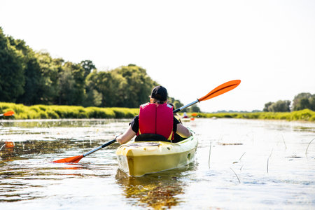 Back view of a person kayaking on a vibrant river, immersed in serene natureの写真素材