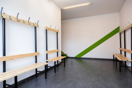 Modern Locker Room with Vibrant Green and White Striped Walls, Wooden Benches, and Coat Hooksの写真素材