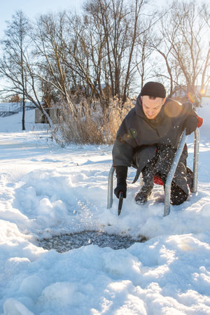 Man carving out a hole in the ice with an axe for winter swimming in cold sunny winter dayの写真素材