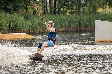 Young man wakeboarding and doing different board tricks. Wake boarding sportsman man jumping high wake boarding raley trick with huge water splash in the cable parkの写真素材