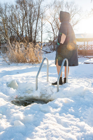 Man standing by a winter swimming hole, ready to embrace the cold in a snowy landscapeの写真素材