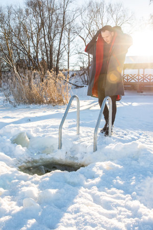 Winter swimmer wrapped in a red towel after a refreshing dip in a snowy ice holeの写真素材