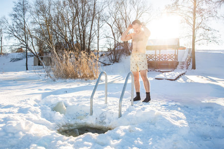 Young man enjoying winter swimming in a hand-cut ice hole on a sunny snowy dayの写真素材