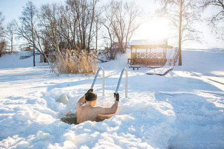 Man embracing the cold in an ice swimming hole during a sunny winter dayの写真素材