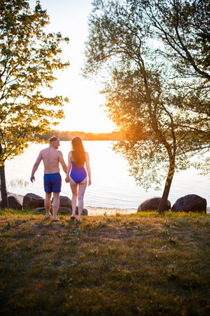 couple enjoying a romantic sunset by the lakeside, framed by trees with golden sunlight reflecting on tranquil watersの写真素材