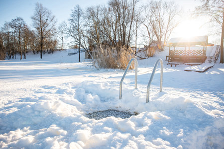 Idyllic winter swimming spot with hole and metal ladder on a snowy lakeside at sunriseの写真素材
