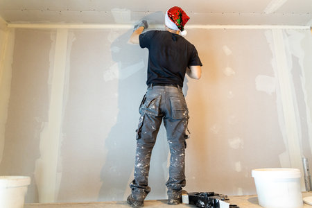 Professional painter in Santa hat applying plaster on wall for home renovationの写真素材