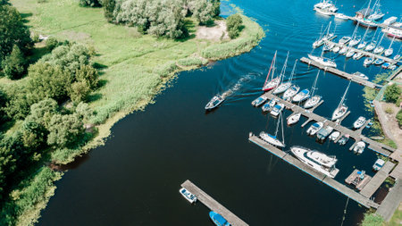 Aerial view of a peaceful marina with various sailboats docked along the pier, surrounded by lush greenery on a bright sunny dayの写真素材
