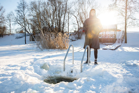 Winter swimming preparation. Man standing by freshly cut ice hole on a snowy lakesideの写真素材