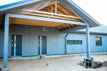 Modern wooden house under construction with blue siding and exposed roof framework on a sunny dayの写真素材