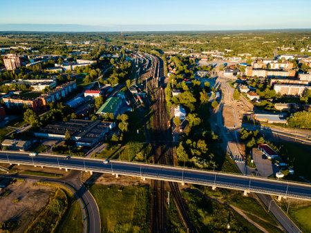 Serene Urban Escape: Green Fields Meet Sunlit Roads and Railways in Aerial Viewの写真素材