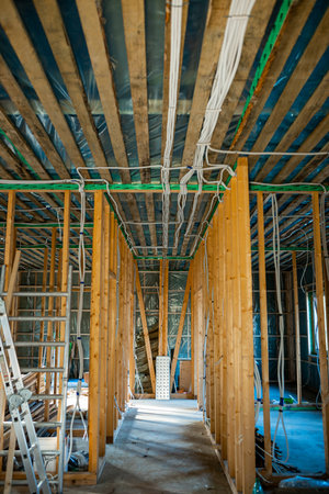 Under-construction home interior with wooden framing, electrical wiring, and ladder on siteの写真素材