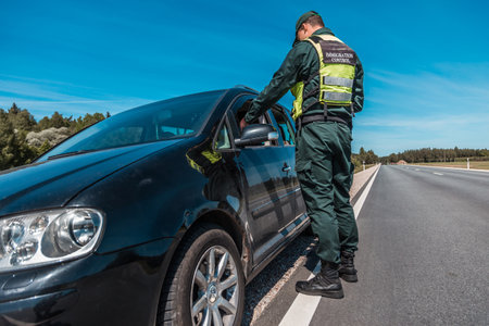 border patrol officer inspecting vehicle at checkpoint on sunny day with clear skies and long open roadの写真素材