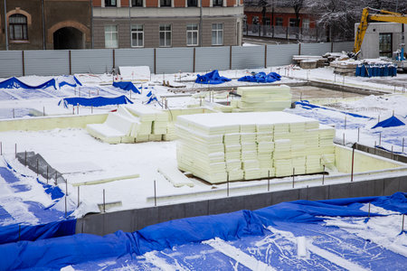 construction site in winter with stacks of insulation boards and blue protective tarps against snowの写真素材