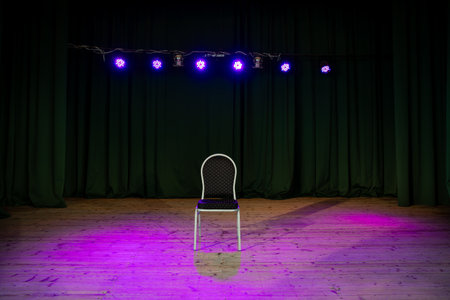 solitary chair on a stage bathed in purple spotlight with dark green curtains in the background, awaiting a performerの写真素材