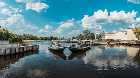 Panoramic view of speed boats docked at a tranquil marina with sailing yachts under a blue sky with fluffy cloudsの写真素材