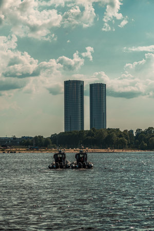 Two military speed boats patrolling the river with a historic city skyline and fluffy white clouds in the backgroundの写真素材