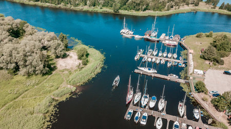 Aerial view of a peaceful marina with various sailboats docked along the pier, surrounded by lush greenery on a bright sunny dayの写真素材