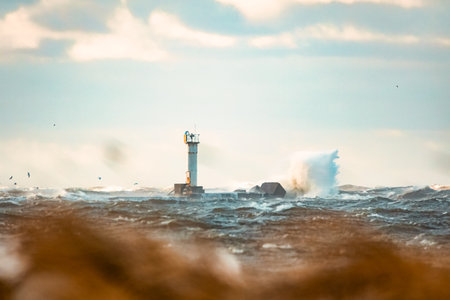 Huge waves crashing down the lighthouse during the storm. Stormy weather by the sea in Riga, Latvia.の写真素材