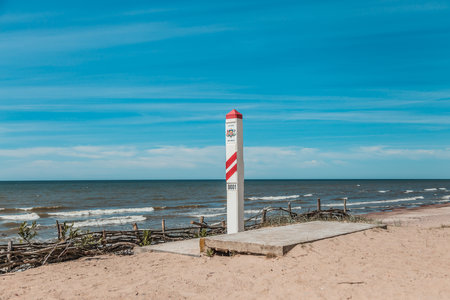 Red and white striped border post marked '0001' on a sunny beach, symbolizing the starting point of the border along the coastlineの写真素材