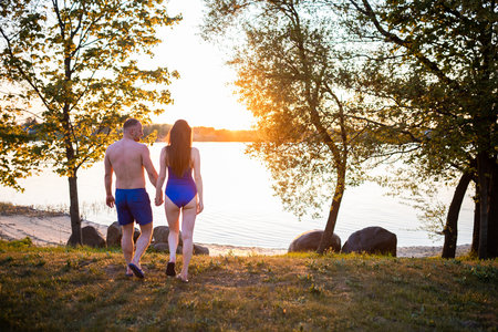 couple enjoying a romantic sunset by the lake, with golden sunlight peeking through the trees on a peaceful eveningの写真素材