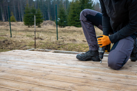 Deck or terrace construction, builder hand with electric screwdriver installing impregnated wooden...