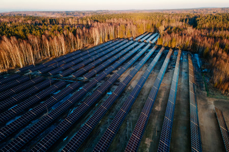 Aerial view of a large solar farm at sunset with rows of photovoltaic panels amidst a natural landscape, showcasing renewable energy.の写真素材