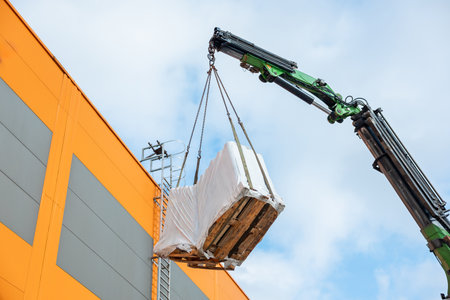 High-Angle View of a Crane Lifting a Wrapped Pallet Against a Blue Skyの写真素材