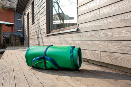 Green Inflatable Stand-Up Paddle Board Rolled Up Next to Wooden House Ready for Summer Funの写真素材