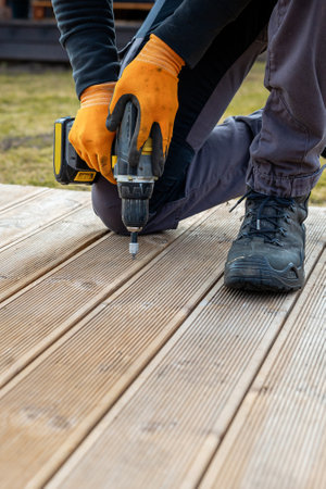 Deck or terrace construction, builder hand with electric screwdriver installing impregnated wooden boardsの写真素材