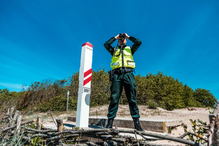 Immigration control officer surveying the coast with binoculars, vigilant in national border protection duties on a sunny dayの写真素材