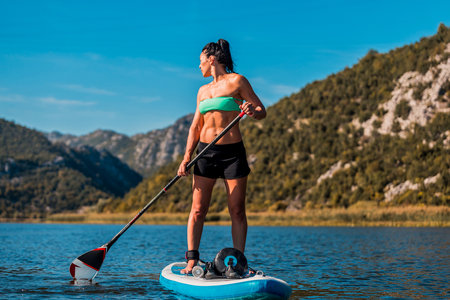 female paddler on inflatable sup board amidst stunning mountainous landscape and turquoise watersの写真素材