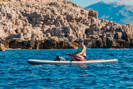 female paddler on inflatable sup board amidst stunning mountainous landscape and turquoise watersの写真素材