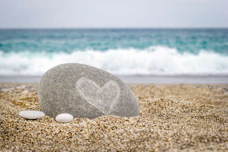 Stone with a heart symbol on the sand of the sea beachの写真素材