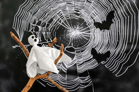 White ghost sits on branch against background of cobwebs and bats. Concept of halloween .の写真素材