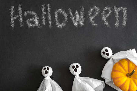 Halloween concept, three ghosts with pumpkin on black background with inscription Halloween. Top view.の写真素材