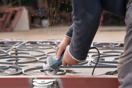 Man grinds metal fence with angle grinder. Side view