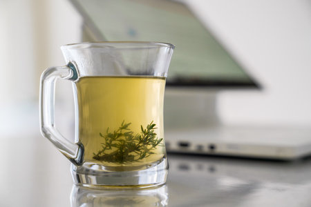 Glass transparent cup with herbal tea with grass leaves on the background of a working computer. Concept of work at home and rest break during work.の写真素材