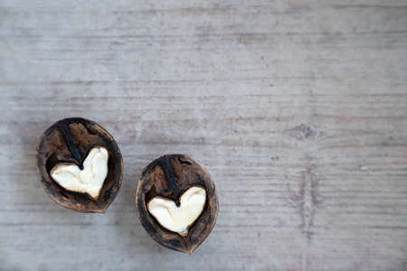 Two halves of split walnut with core in form of white hearts on wooden background. Concept of Valentines Day and health. Copy space.の写真素材